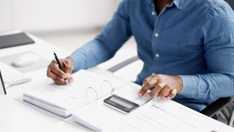 Man sitting at a desk using a calculator to work on an accounting task