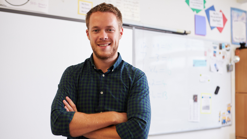 Teach stood with crossed arms in front of a white board in a classroom.